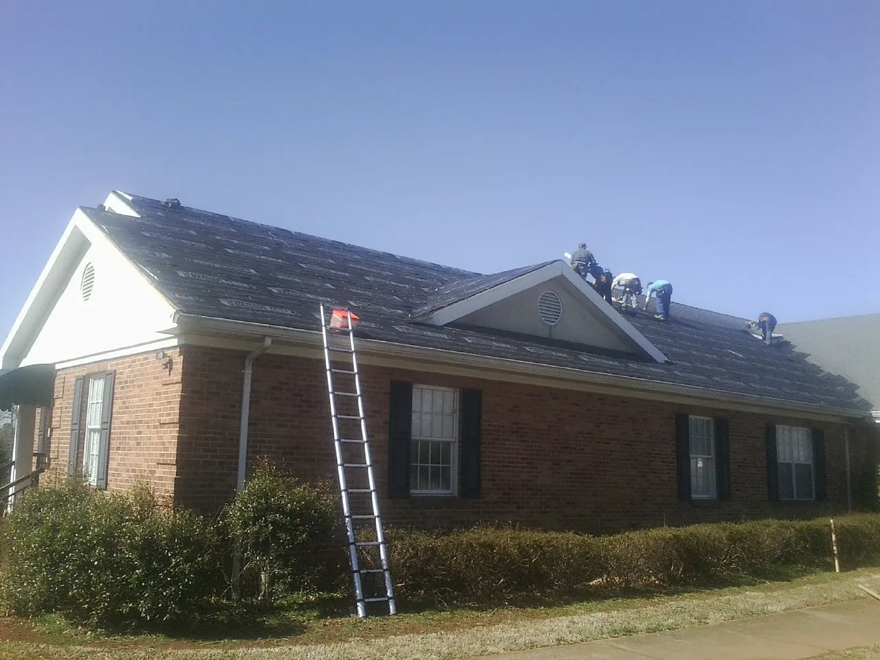 Crew tearing shingles off a brick ranch roof with a ladder set — Metal Roof Repair work by our crew in Glen Spey