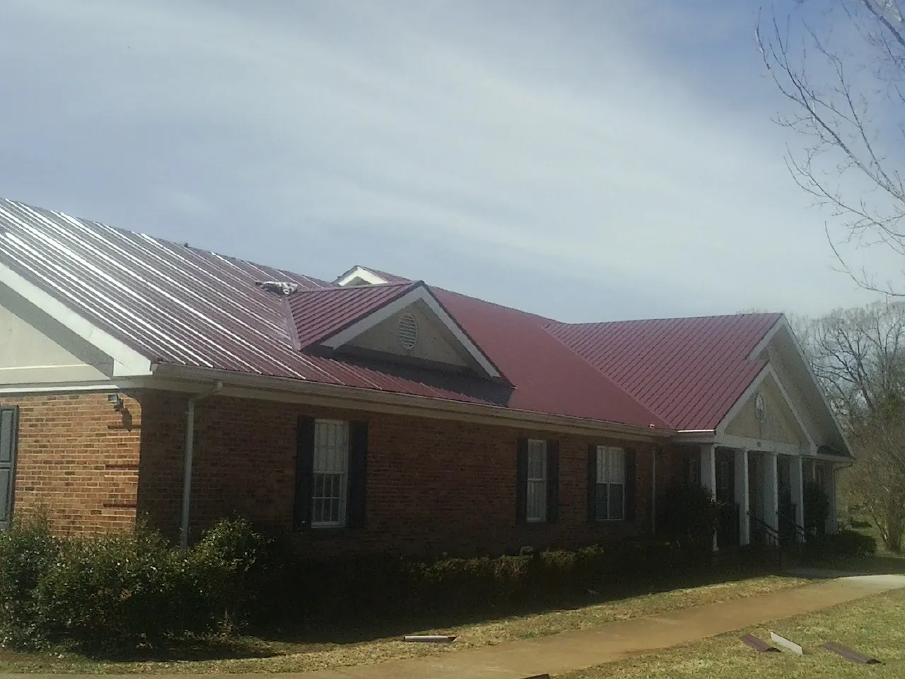 Red metal roof with gabled entries on a long brick building, from a Hail Damage Roof Repair job in Glen Spey