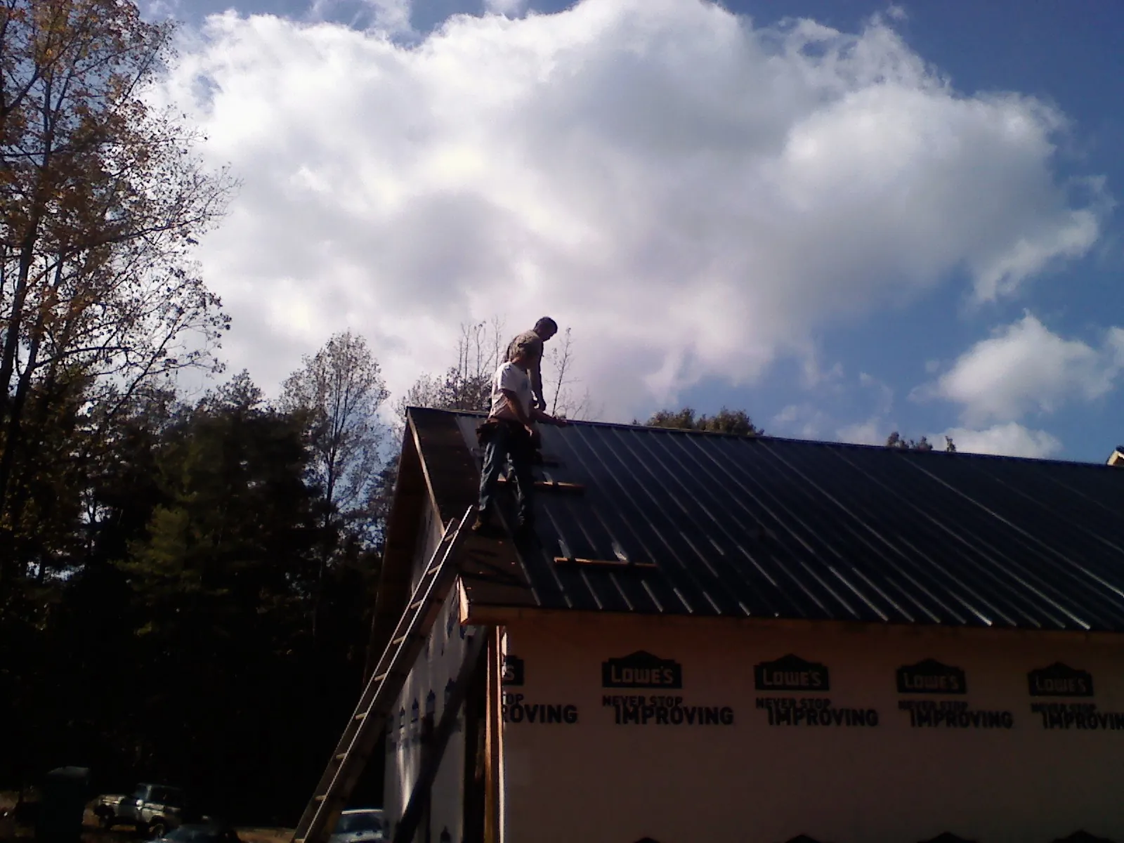 Roofer fastening dark metal panels high against a cloudy sky, from a Roof Inspection job in Glen Spey