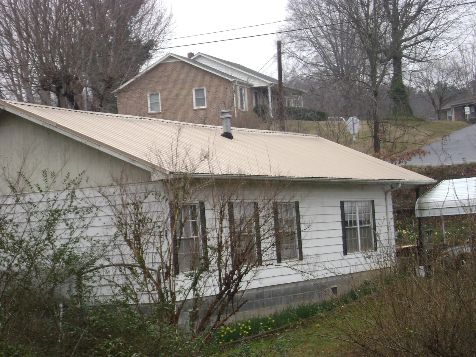 Tan metal roof on a white sided house set into a hillside — Commercial Roofing by Roofing Brothers in Glen Spey